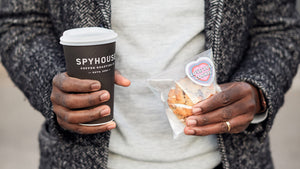 Close-up image of hands holding spyhouse to-go coffee cup and Love You cookie